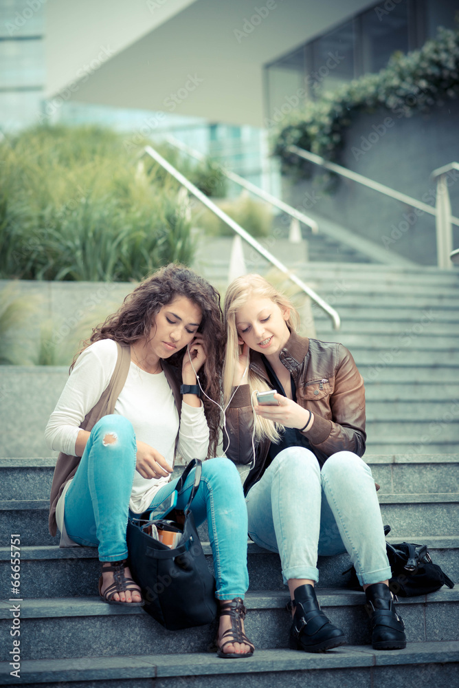 Young women using smartphones and listening to music while sitting on steps