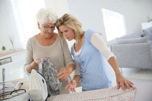 Elderly woman with housekeeper ironing clothes