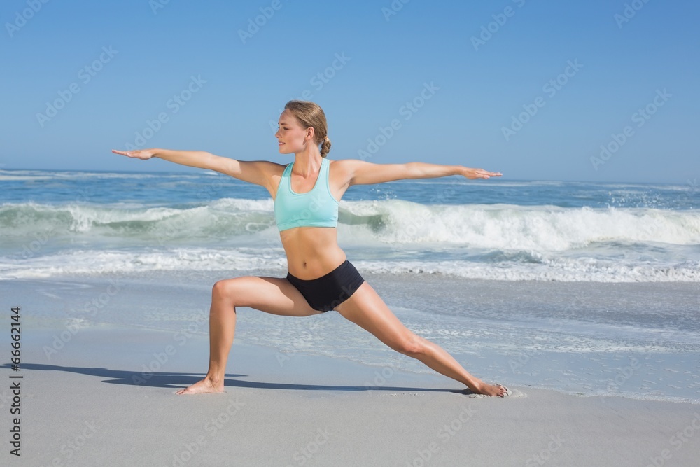 Fit woman standing on the beach in warrior pose Fit woman standing on the beach in warrior pose