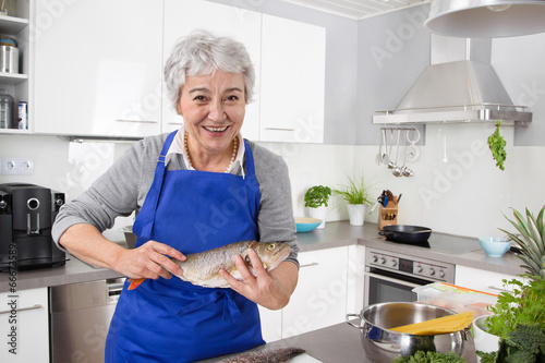 Canvas Print Happy senior woman in the kitchen preparing fresh fish.