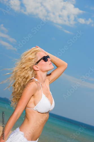 Young woman in white bikini holding sarong on the beach