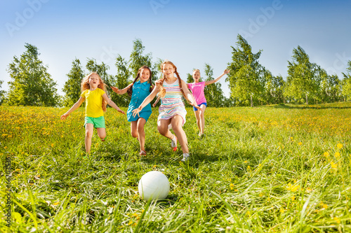 Group of children running to the ball in meadow