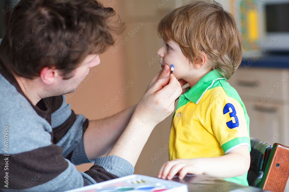 Father painting brazilian flag on face of little son Father painting brazilian flag on face of little son