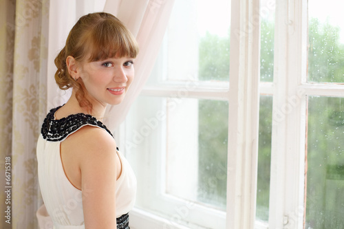 Beautiful smiling girl in white dress near window