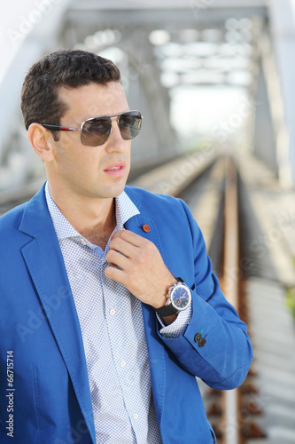 Handsome man in blue jacket and sunglasses stands on railroad photo