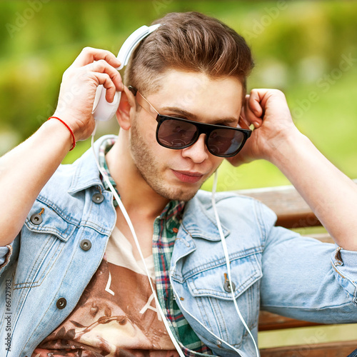 handsome fashion man listening to music on the grass in the park
