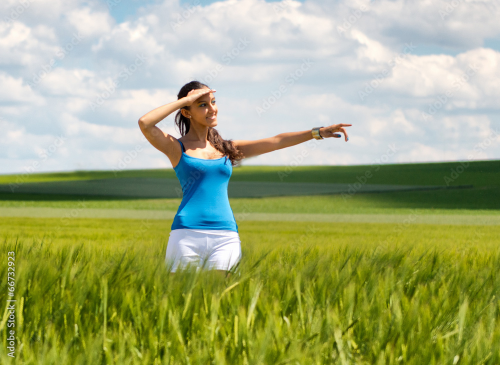 Happy young woman standing in a field pointing Happy young woman standing in a field pointing