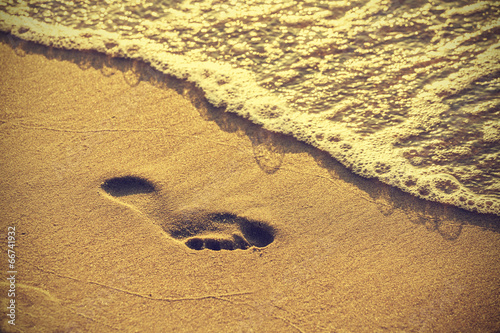 Footprint on sandy beach along the edge of sea, vintage retro style.