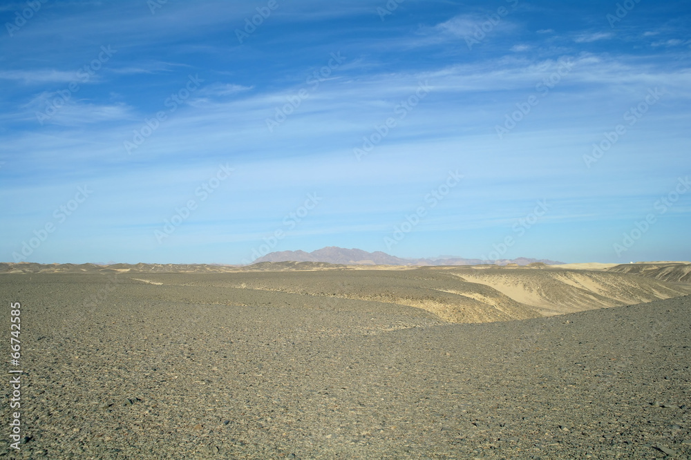 Egyptian desert covered by black stones and blue sky.