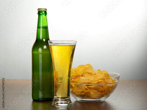 Beer bottle, bowl with chips and a damp glass