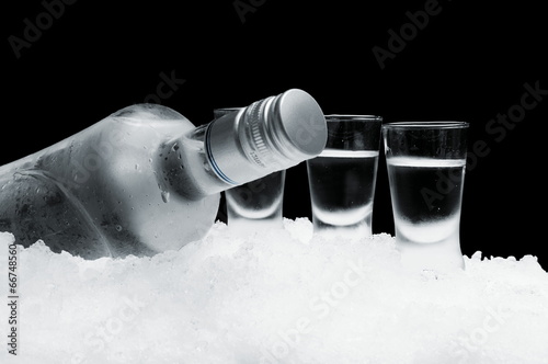 Konstfotografi Bottle of vodka with glasses standing on ice on black background