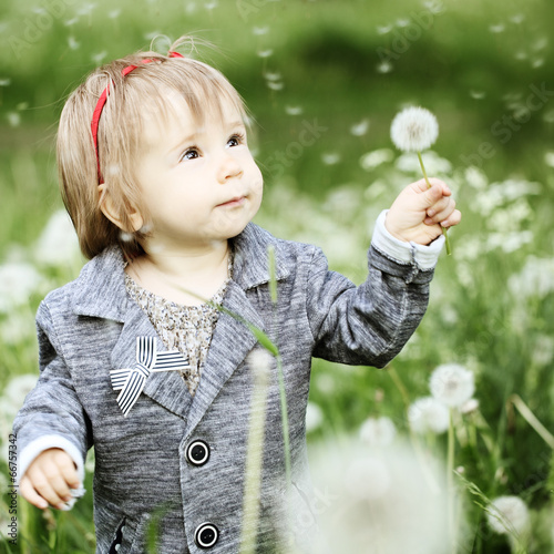 Smiling baby girl with dandelion on green grass
