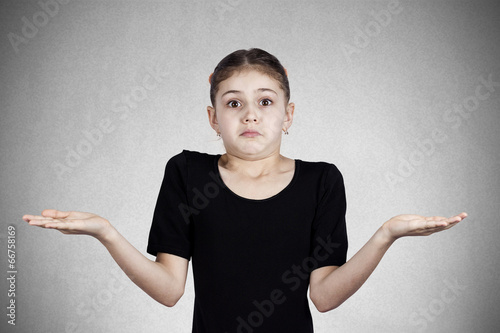 Foto Confused, annoyed little girl shrugs shoulders, grey background