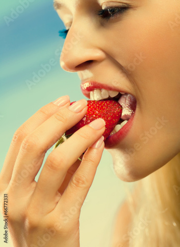 Young woman eating strawberry on sea beach