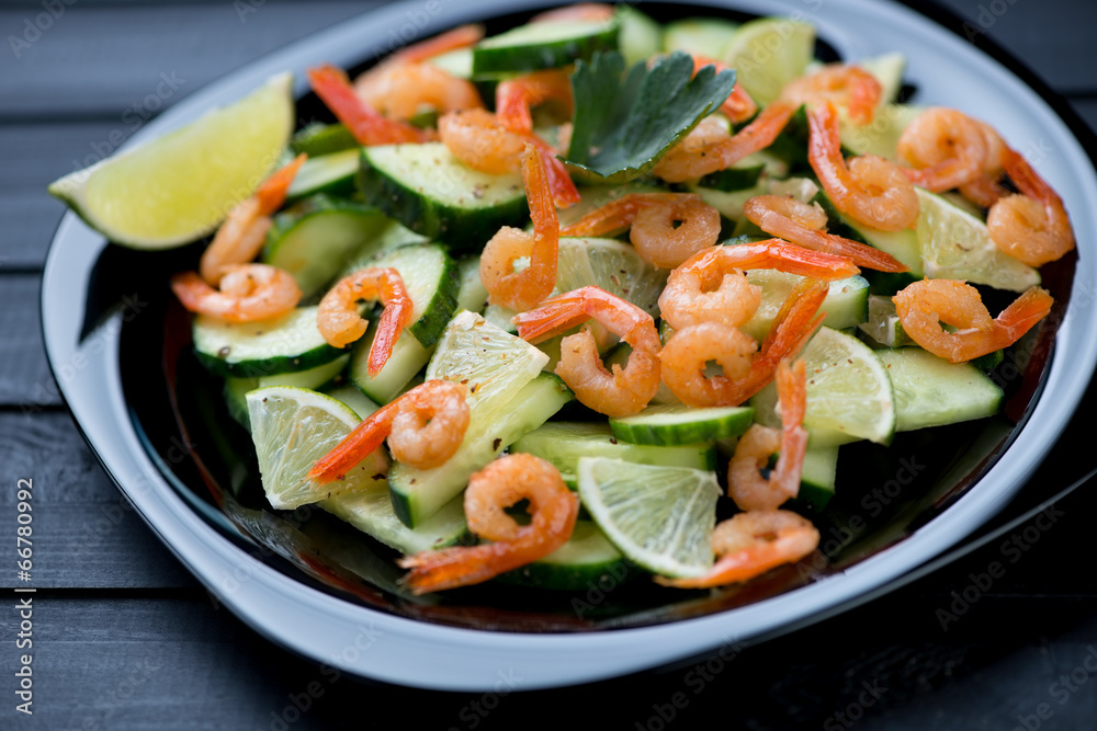 Black plate with fried shrimp, lime and cucumber salad