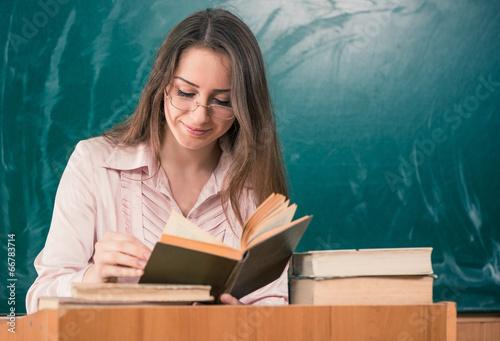 female techer reading book at blackboard