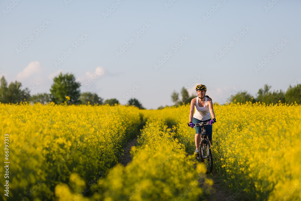 Woman is cycling in yellow rapeseed field