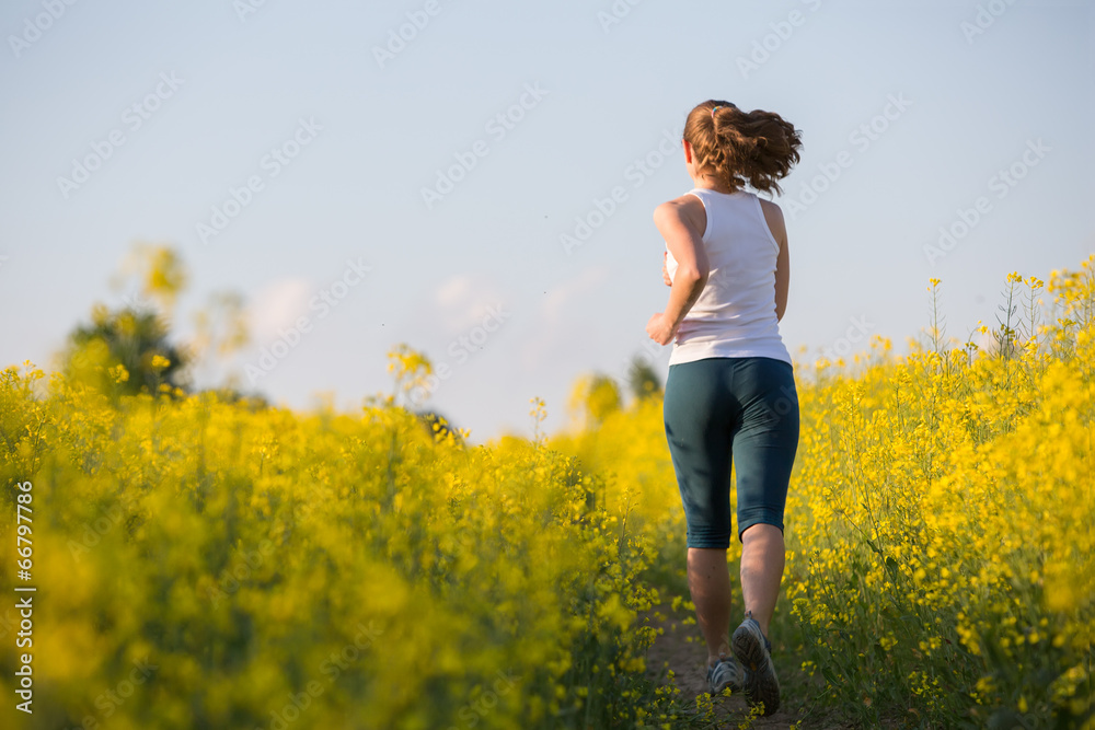 Young woman is jogging in yellow rapeseed field at sunset Young woman is jogging in yellow rapeseed field at sunset
