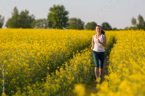 Young woman is jogging in yellow rapeseed field at sunset