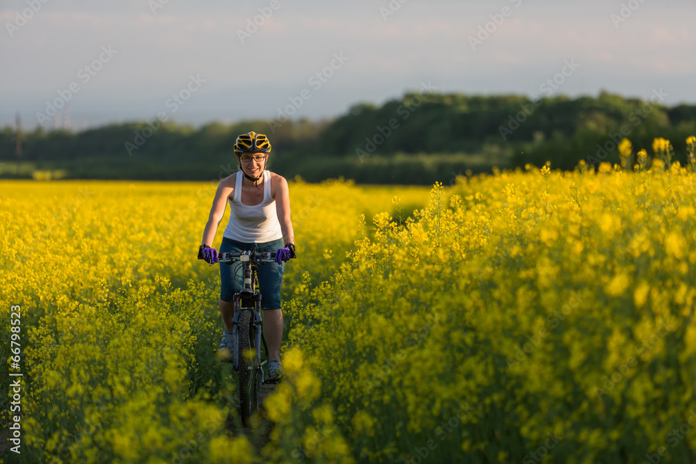 Woman is cycling in yellow rapeseed field