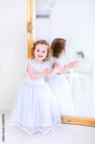 Little girl in a white dress next to a mirror