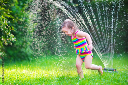 Adorable girl playing with garden sprinkler photo