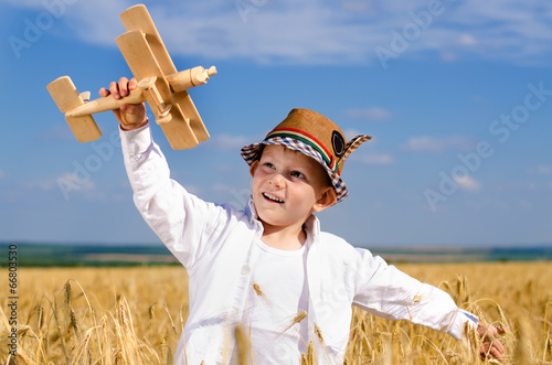 Принти на полотні Little boy flying a toy plane in a wheat field