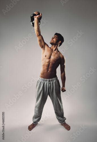 Muscular man doing one arm snatch with kettlebell