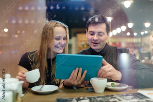 Young people drinking coffee and looking on pad