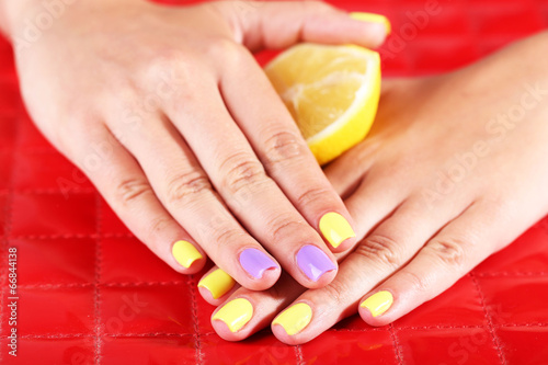 Female hand with stylish colorful nails holding fresh lemon 
