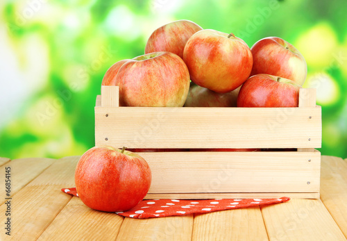 Ripe apples in wooden box, on bright background