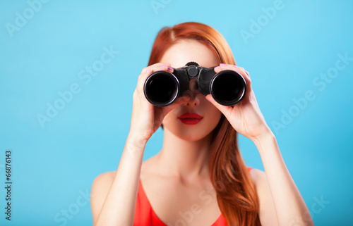 Redhead girl with binocular on blue background.