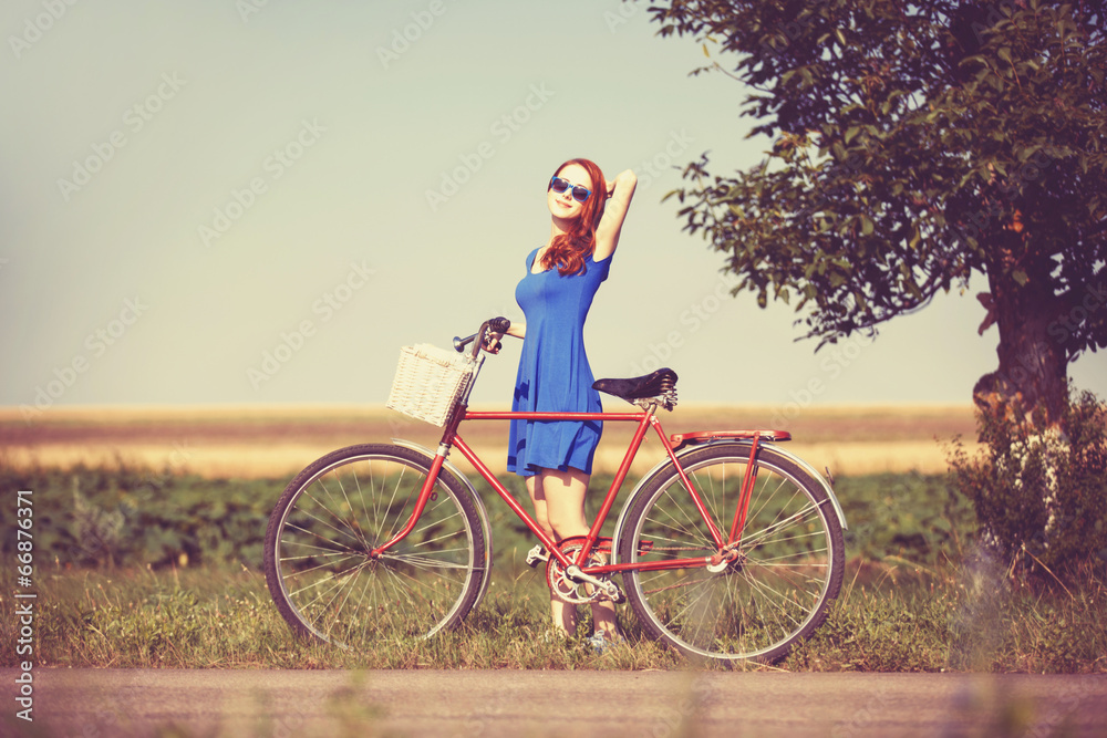 Fototapeta premium Redhead girl with bicycle on country road.