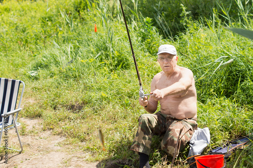 Elderly fisherman reeling in a small fish