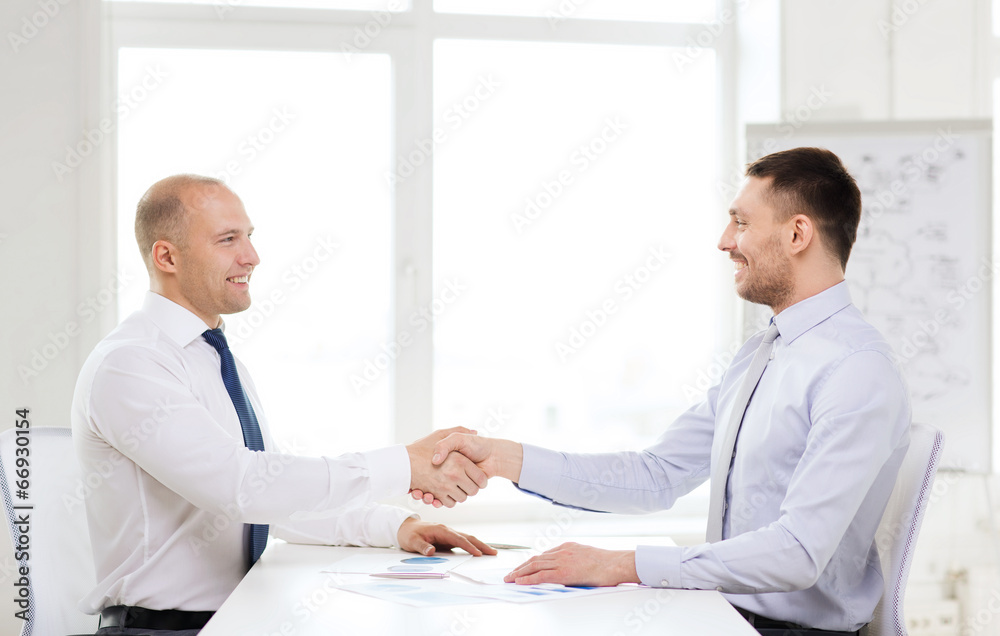 two smiling businessmen shaking hands in office two smiling businessmen shaking hands in office