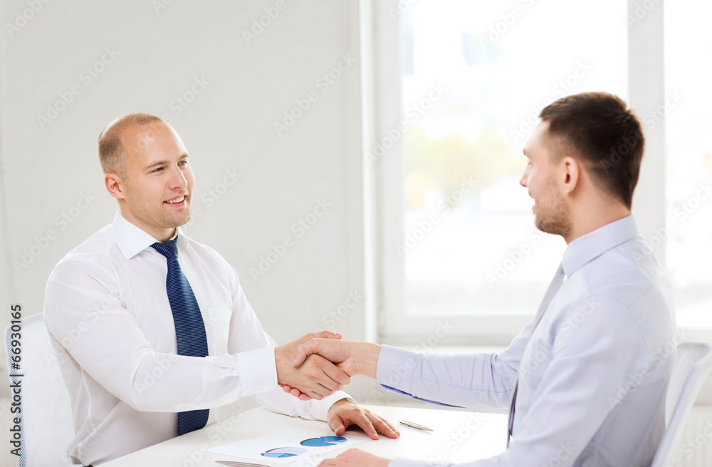 two smiling businessmen shaking hands in office two smiling businessmen shaking hands in office
