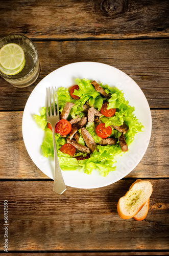 green salad with tomatoes and roast beef in a white dish