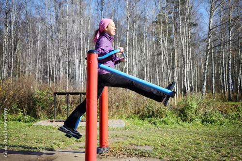 Fototapeta Naklejka Na Ścianę i Meble -  Young happy woman moves at simulator in park in autumn sunny day