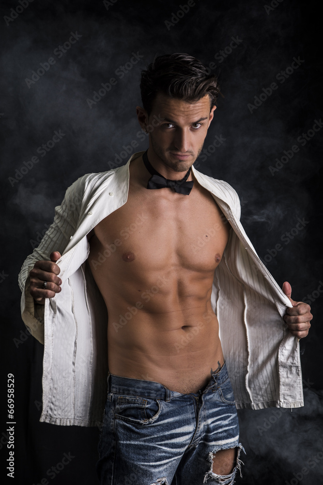 Fototapeta premium Handsome lean, man in jeans taking off shir