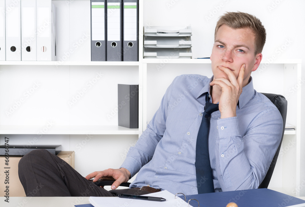 Naklejka premium Junger nachdenklicher Mann sitzt am Schreibtisch im Büro