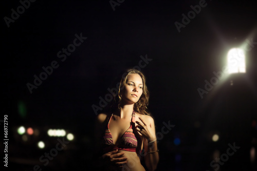 Young beautiful woman in bikini against night on beach near