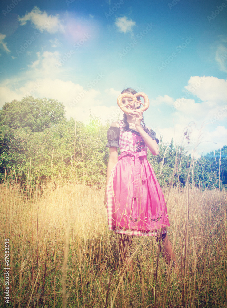 Bavarian girl wears a dirndl and holds a brezel Bavarian girl wears a dirndl and holds a brezel