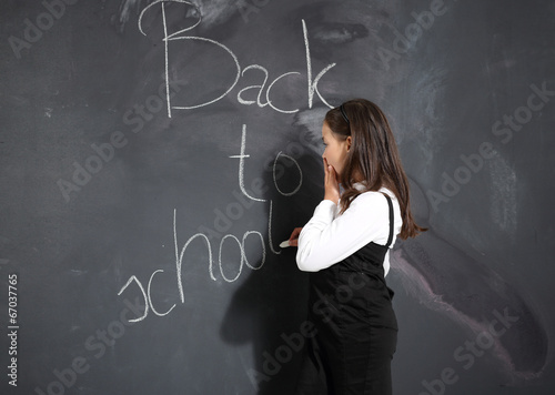 dziewczynka stoi przy czarnej szkolnej tablicy