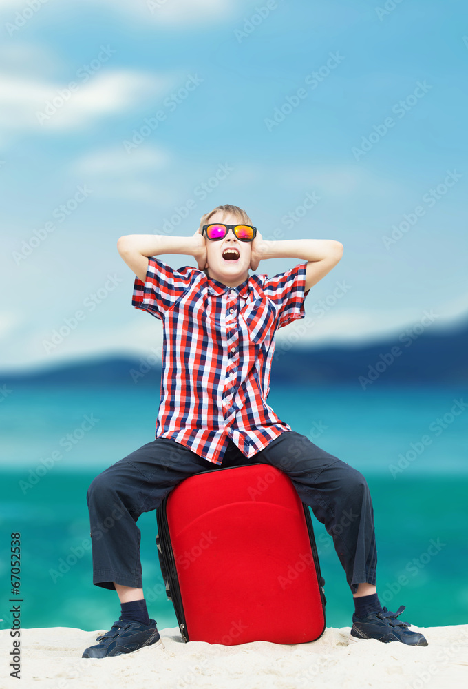 Fototapeta premium Boy sitting with his luggage at the beach and screaming