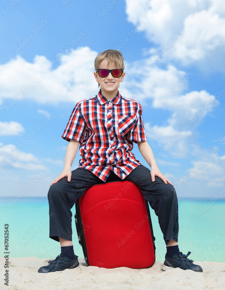 Fototapeta premium Happy boy with his luggage, tropical beach background