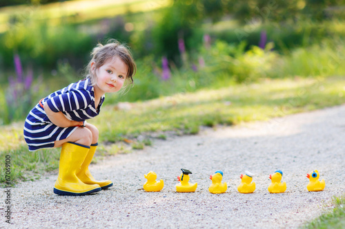 Fotografie Adorable little girl with rubber ducks in summer park