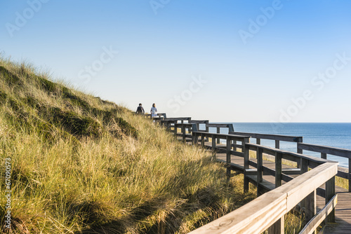 People on wooden footpath on dune at beach in Germany.