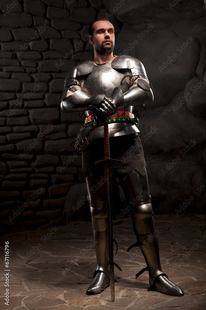 Medieval Knight posing with sword in a dark stone background Medieval Knight posing with sword in a dark stone background