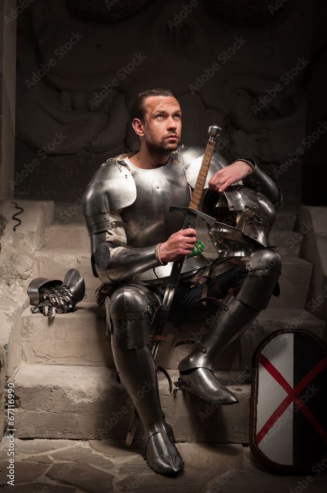 Medieval knight sitting on the steps of ancient temple Medieval knight sitting on the steps of ancient temple