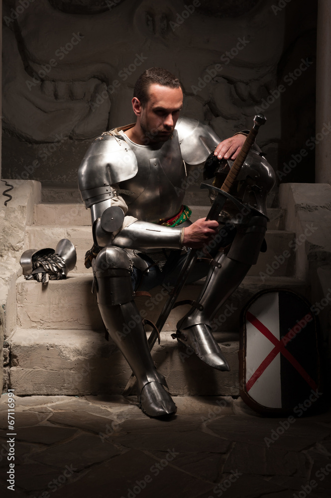 Medieval knight sitting on the steps of ancient temple Medieval knight sitting on the steps of ancient temple